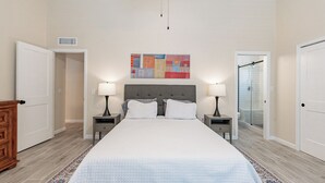 A bedroom with a large bed, two bedside tables with lamps, a gray headboard, a colorful abstract painting above the bed, and a walk-in closet. - Gilbert AZ 4BR Vacation Home Remodeled Garage (Gilbert)