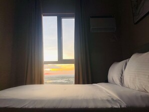 Et hotelværelse med en seng, et vindue med gardiner og en vægmonteret aircondition.