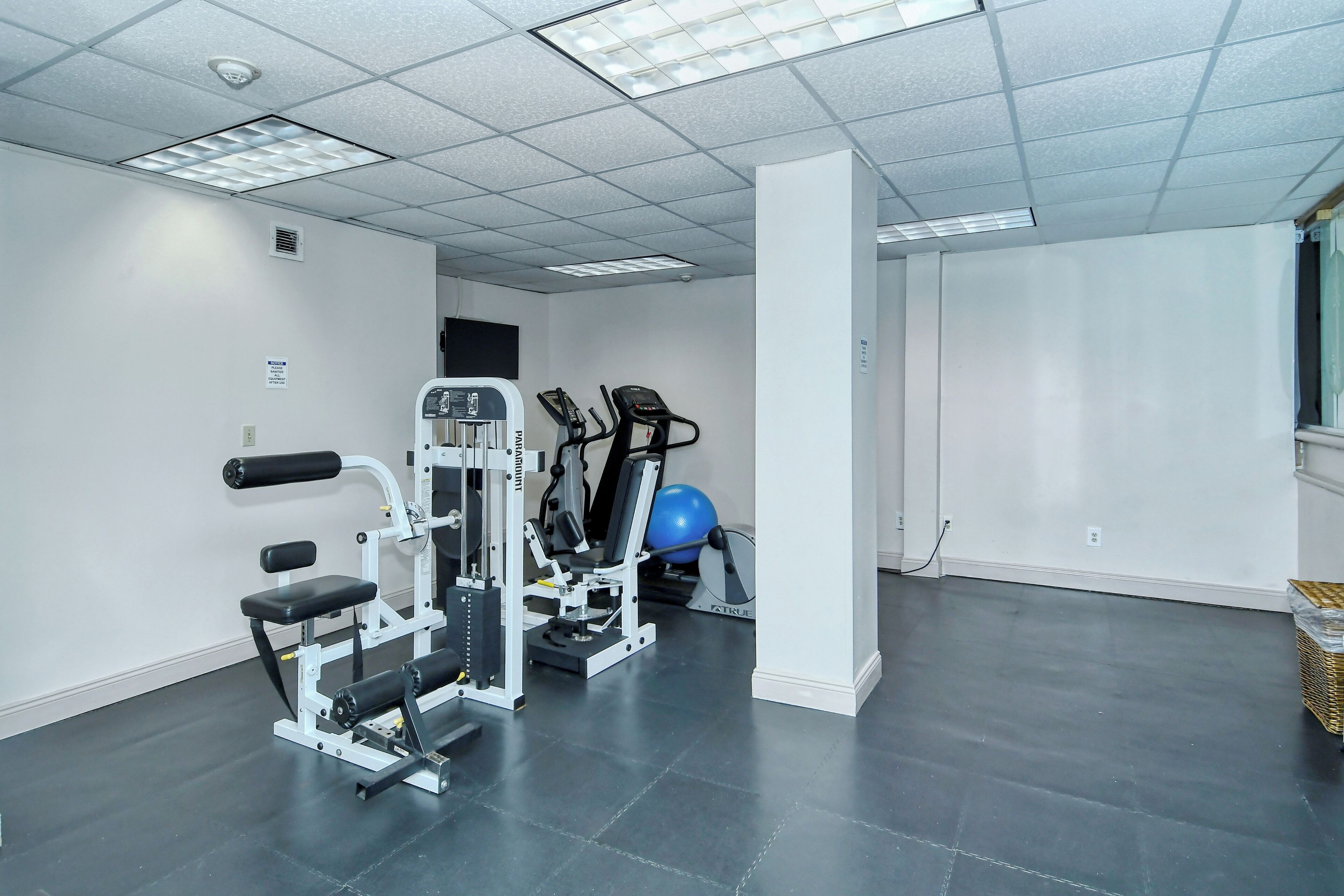 Een sportschool met trainingsapparatuur, een blauwe fitnessbal en een witte pilaar.