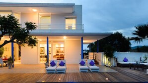 A modern two-story house with a swimming pool, outdoor seating, and a well-lit patio area.
