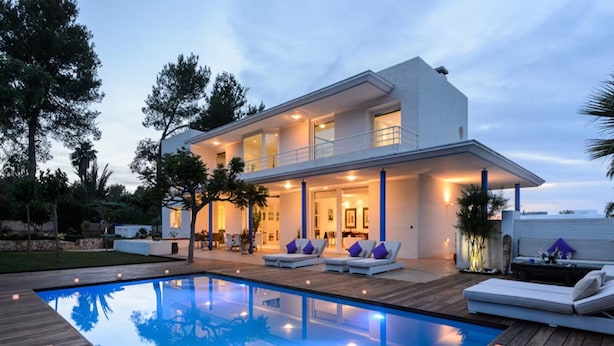 A modern two-story house with a swimming pool, outdoor seating, and a well-lit patio area.