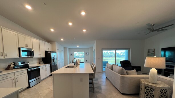 A modern kitchen with white cabinetry, a central island, and a dining area with a sofa and chairs. - 2-bedroom condo  in Wellen Park Golf and Country Club with Golf Membership (Venice)