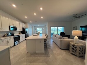 A modern kitchen with white cabinetry, a central island, and a dining area with a sofa and chairs. - 2-bedroom condo  in Wellen Park Golf and Country Club with Golf Membership (Venice)