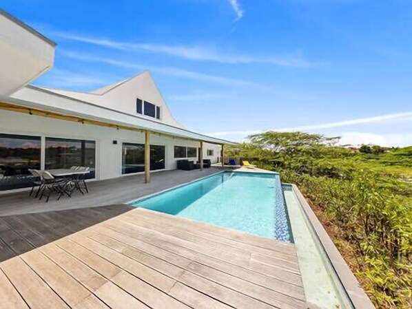 A modern house with a swimming pool, wooden deck, and outdoor seating area.