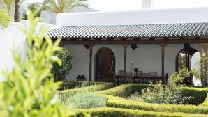 A traditional building with a tiled roof, arched doorways, and a garden with manicured hedges and palm trees. - Amazing Villa With Swimming Pool (San Juan de Alicante)