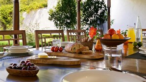 An outdoor dining area with a table set for breakfast, including bread, fruit, and a bottle of juice. - Amazing Villa With Swimming Pool (San Juan de Alicante)