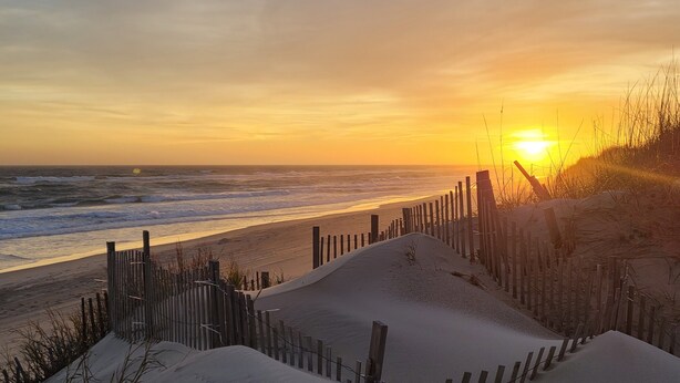 Une plage avec une clôture en bois et des dunes de sable.