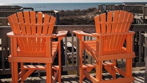 Deux chaises Adirondack orange sont posées sur une terrasse en bois, offrant une vue sur l’océan.