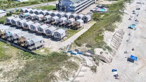Un hôtel situé sur la côte, doté de nombreuses chambres de style bungalow disposées en rangées, d’une piscine et d’un espace de plage agrémenté de parasols.