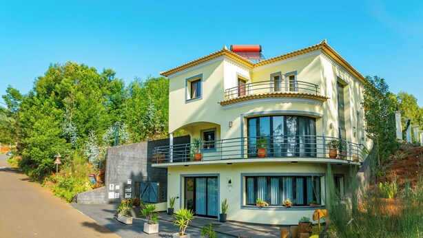 A two-story building with a balcony, potted plants, and a clear sky. - Alpine escape villa Vienna apt Gaula Madeira  (Gaula)