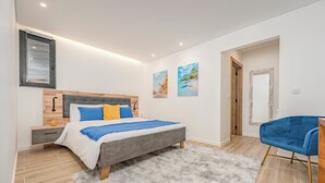 Un dormitorio moderno con cama, mesitas de noche, una silla azul y obras de arte en las paredes.