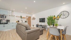 Una cocina moderna con horno empotrado y microondas, un comedor con mesa y sillas, y una sala de estar con sofá.