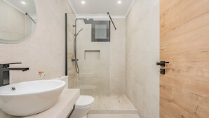 Un baño moderno con un lavamanos grande blanco, un inodoro y una zona de ducha con mampara de vidrio.