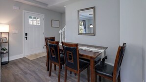 A dining area with a wooden table and chairs, a mirror on the wall, and a door with a window.