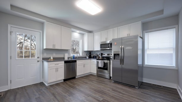 A modern kitchen with white cabinets, stainless steel appliances, and a wood floor.