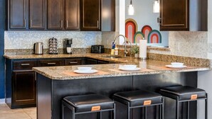 A modern kitchen with dark wood cabinets, granite countertops, and a central island with stools. - The Ultimate Getaway: Pool, Pickleball, Mini Golf (San Antonio)