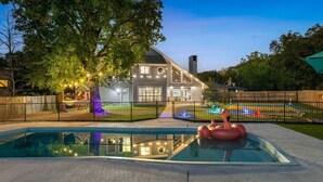 A house with a swimming pool, a flamingo float, and a fenced yard with colorful lights. - The Ultimate Getaway: Pool, Pickleball, Mini Golf (San Antonio)