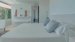 Un dormitorio moderno con una cama grande, un banco empotrado y vistas a zonas verdes.
