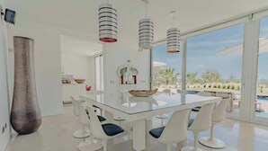 Un comedor moderno con una mesa de vidrio, sillas blancas y lámparas colgantes.