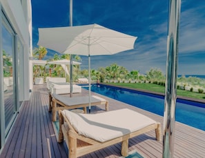 A wooden deck with lounge chairs and umbrellas overlooking a swimming pool. - Modern Villa With Indoor Pool (Sant Josep de sa Talaia)