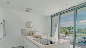 Una cocina moderna con una isla grande, horno empotrado y vistas a una piscina a través de puertas correderas de vidrio.