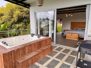 A modern outdoor bathroom with a wooden bench, a hot tub, and a glass door leading to a bedroom with a bed and a wooden headboard. - Alto del sion peñol guatape (El Peñol)