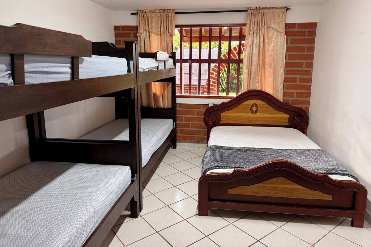 A room with bunk beds and a single bed, a window with curtains, and a brick wall.