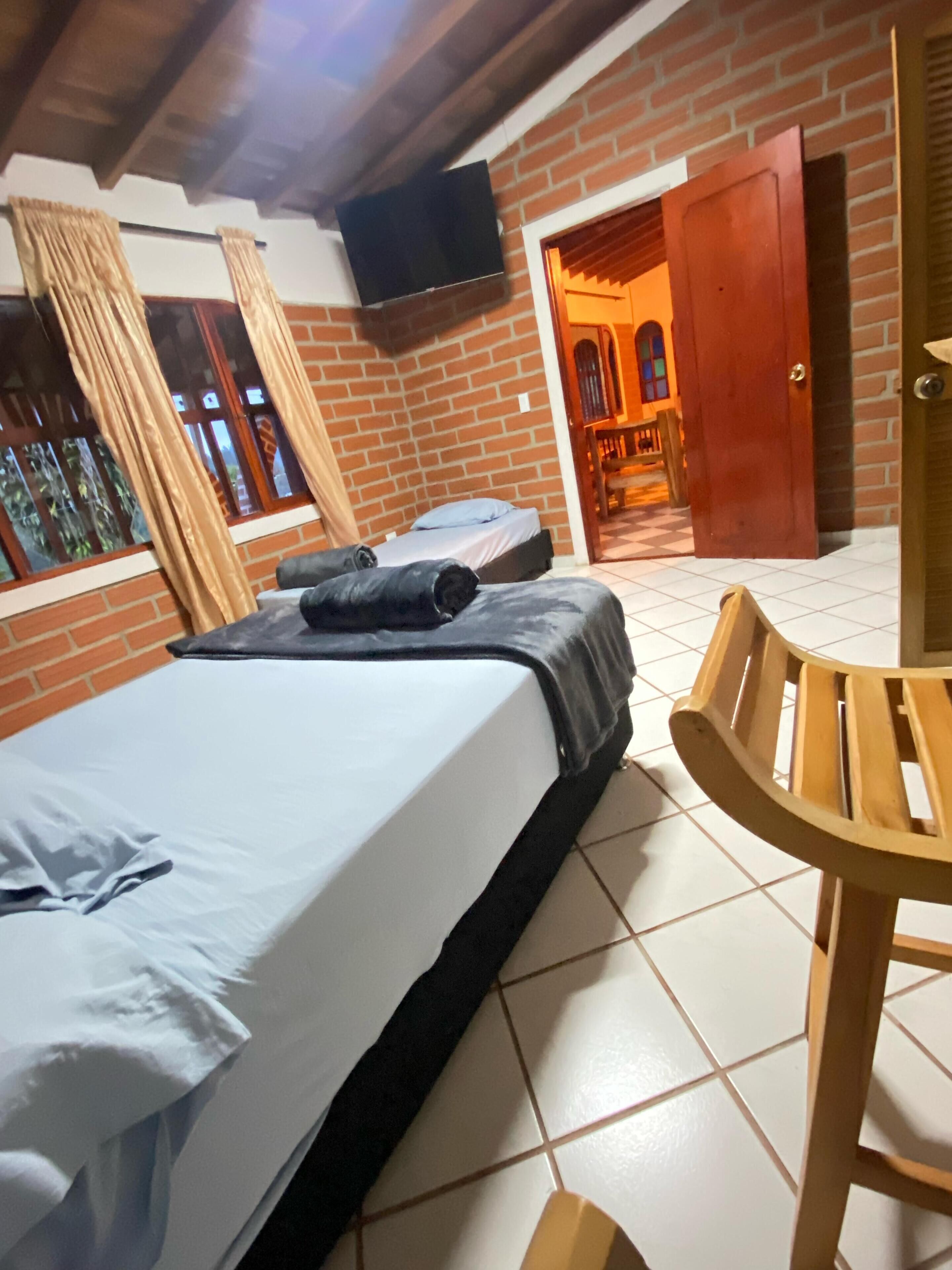Una habitación con una cama, una silla, un televisor y una puerta que da a otra habitación.