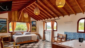 A room with a bed, a wooden bench, a bathtub, and a view of greenery through the windows. - Alto del sion  peñol guatape  (El Peñol)
