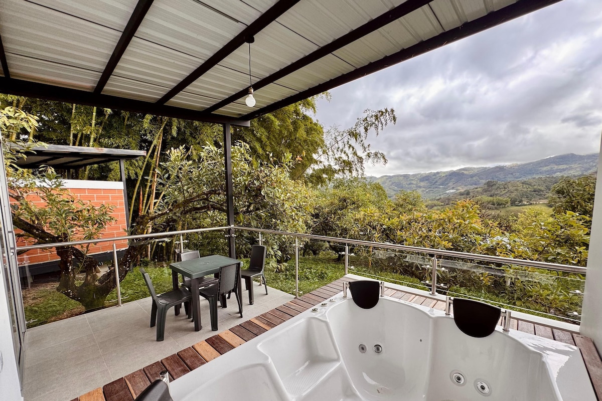 A covered outdoor area with a hot tub, seating, and a view of a mountainous landscape.
