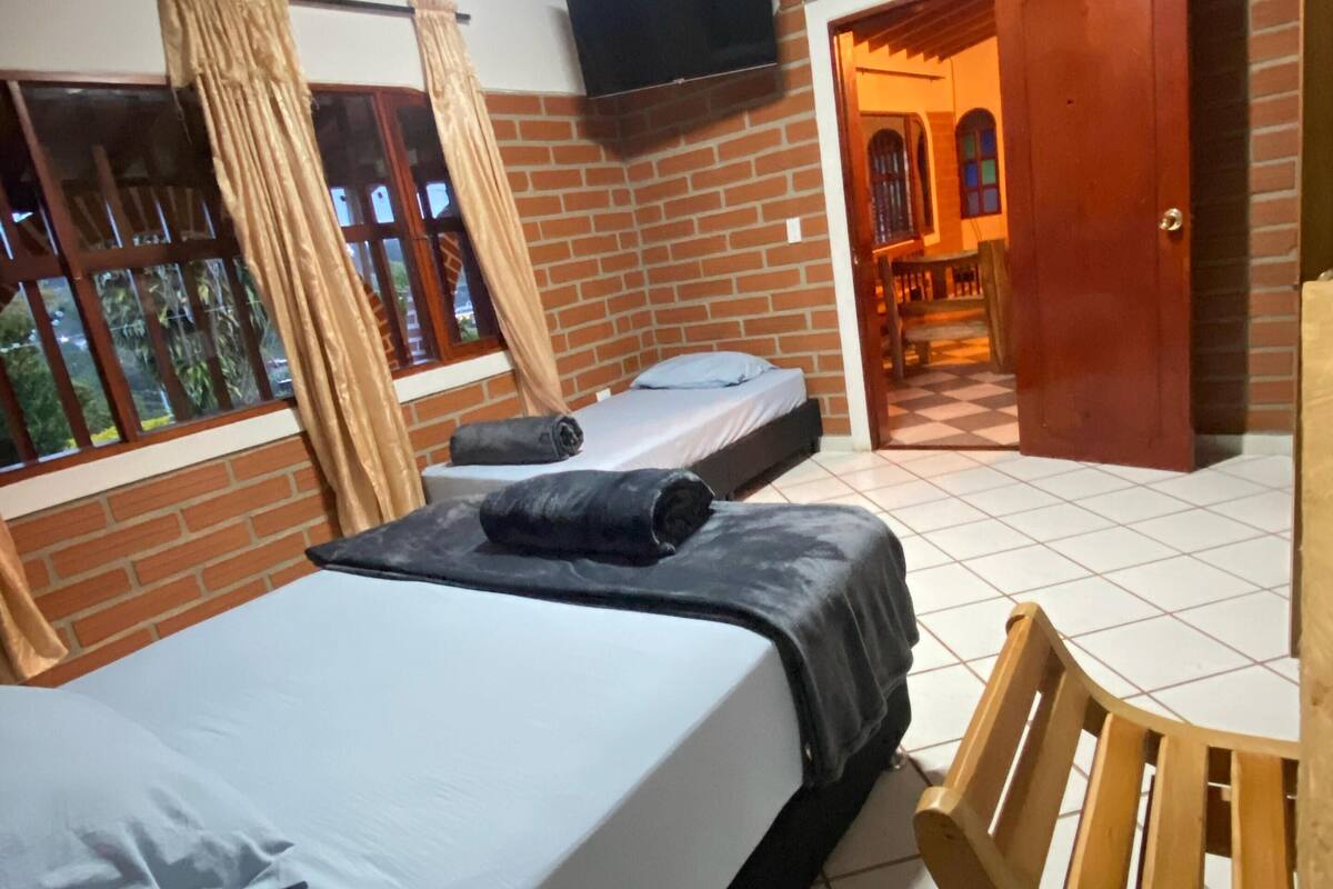 A room with two beds, a wooden chair, a television, and a brick wall.