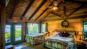 A wooden cabin bedroom with a stone bathtub, a bed with a metal frame, and a ceiling fan.