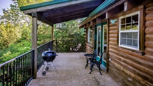 A wooden cabin with a covered porch, a grill, and outdoor seating.