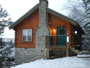 A log cabin with a chimney, a porch, and a green door.
