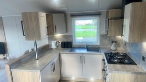 A modern kitchen with a built-in stove, a sink, and wooden cabinets. - Charming 2-bed Chalet in Tuxford (Newark)