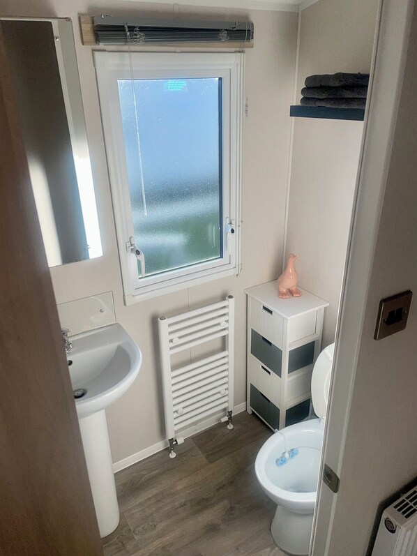 A compact bathroom with a window, a sink, a toilet, and a radiator. - Charming 2-bed Chalet in Tuxford (Newark)