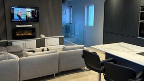Een moderne woonkamer met een grijze bank, een televisie, een open haard en een keuken met een bar.