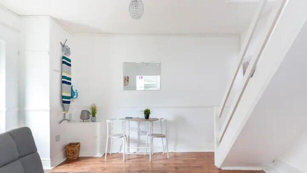 A bright room with a wooden floor, a grey sofa, a small table with chairs, and a hanging plant. - Cheerful Maisonette in the Heart of Orrell Park (Liverpool)