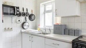 A kitchen with white cabinets, a microwave, a stove, and various pots and pans hanging on the wall. - Cheerful Maisonette in the Heart of Orrell Park (Liverpool)
