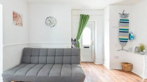 A modern living room with a grey sectional sofa, a clock on the wall, and a striped tie on a stand. - Cheerful Maisonette in the Heart of Orrell Park (Liverpool)