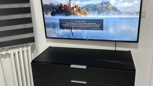 Un téléviseur à écran plat fixé au mur, au-dessus d’un meuble noir pour appareils électroniques, doté de tiroirs.