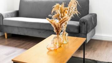 A modern living room with a grey sofa, a wooden coffee table, and two clear glass vases with dried plants.