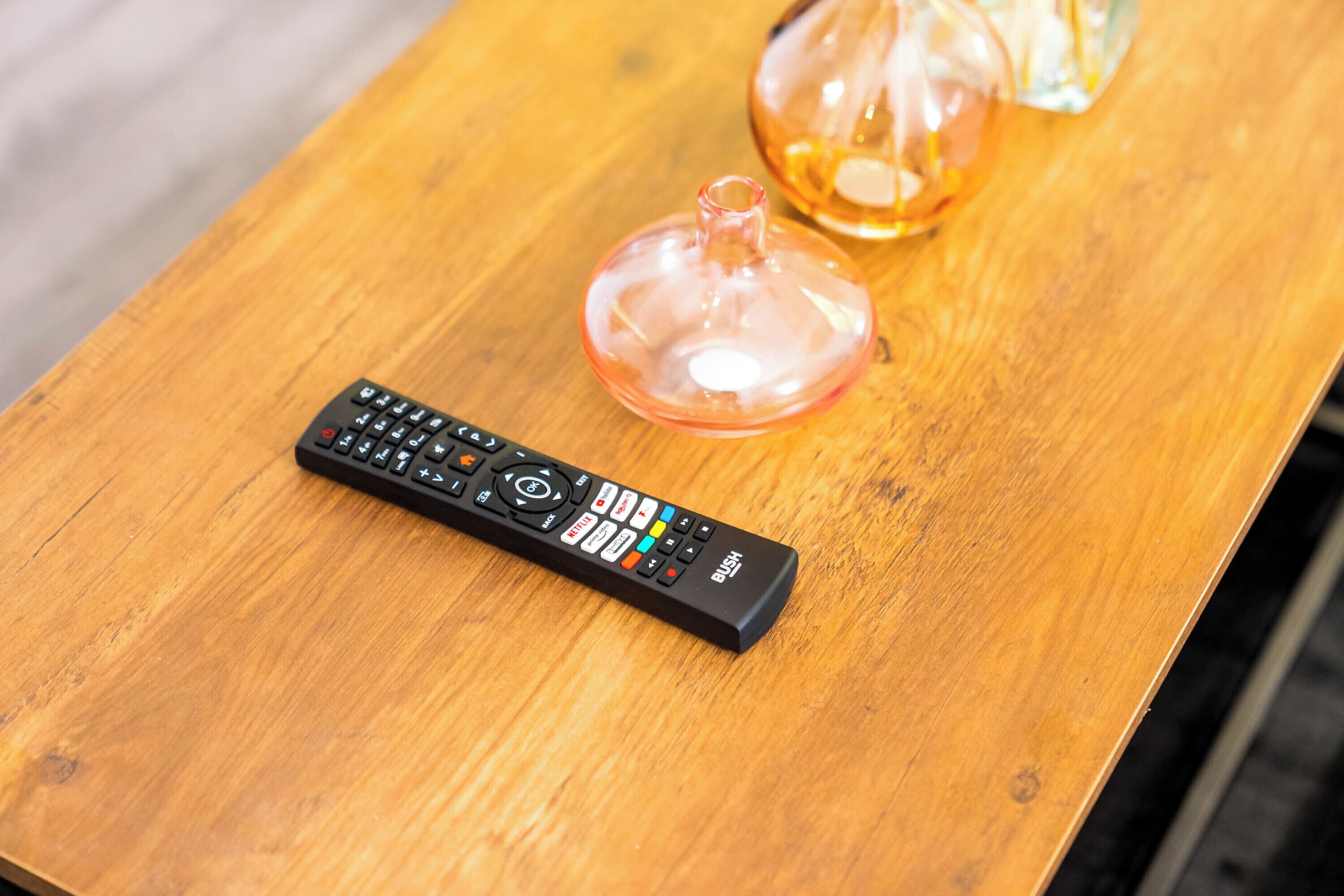 A remote control and a glass vase on a wooden table.