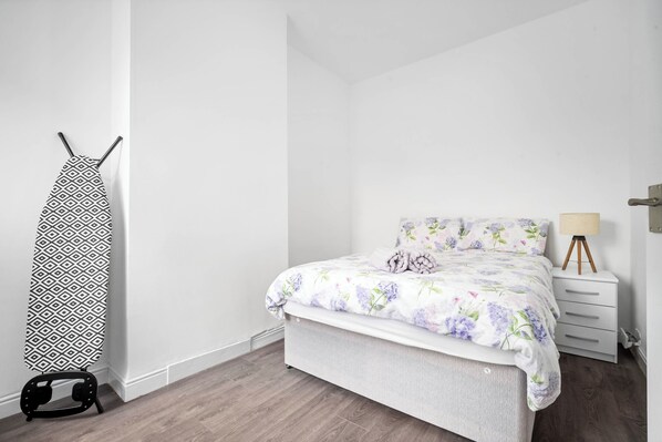 A bedroom with a bed, a dresser, a lamp, and an ironing board. - Apartment 1 Bedroom,sleeps6,parking (Birmingham)