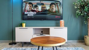 A living room with a TV displaying 'Bromley Boys' on Netflix, a white entertainment unit, a round wooden coffee table, and a blue patterned rug. - Sheffield City Escape - Modern Apartment (Sheffield)