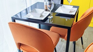 A modern dining area with a glass table, two orange chairs, and a wine glass. - Sheffield City Escape - Modern Apartment (Sheffield)