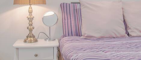 A bedroom with a bed, a bedside table with a lamp, a mirror, and two wall art pieces.