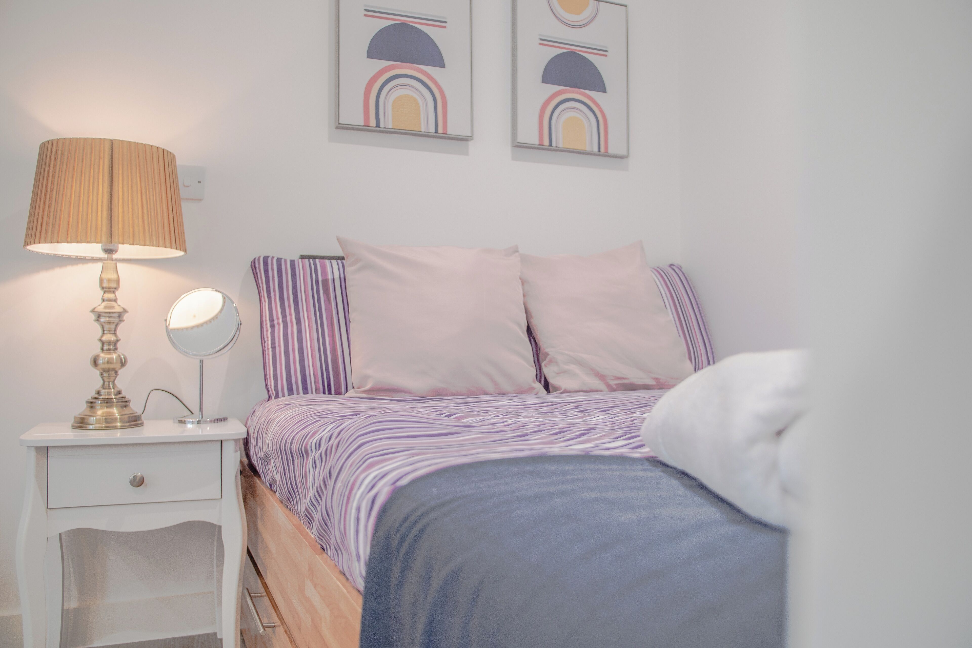 Ein Schlafzimmer mit einem Bett, einem Nachttisch mit Lampe, einem Spiegel und zwei Wandbildern.
