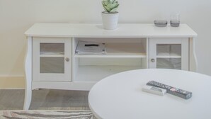 A flat-screen TV mounted on a white wall, a white cabinet below it, and a round table with a remote control on it. - Chic and Cheerful pad in Sheffield City (Sheffield)