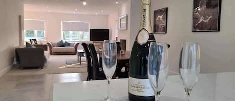A modern living room with a dining area, a large window, and a bottle of champagne on a marble table.